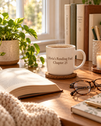 Personalized reading mug on a wooden desk with an open book, glasses and a plant in morning light