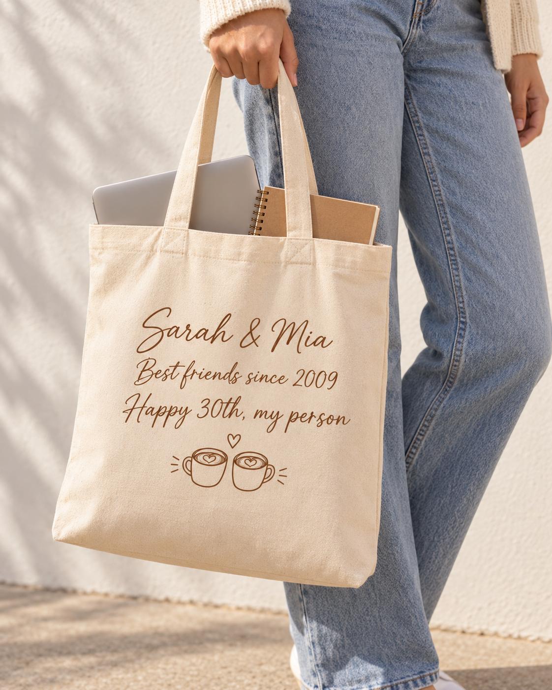 Woman holding the Our Story personalized tote bag with a laptop and notebook inside, showing its size