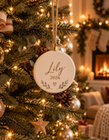Personalized ceramic Christmas ornament with custom name and year hanging on a lit Christmas tree